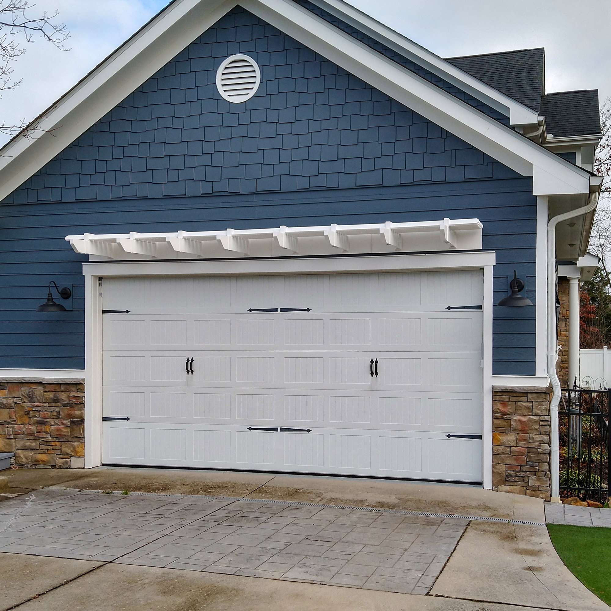 White attached wall pergola above double garage door on blue house