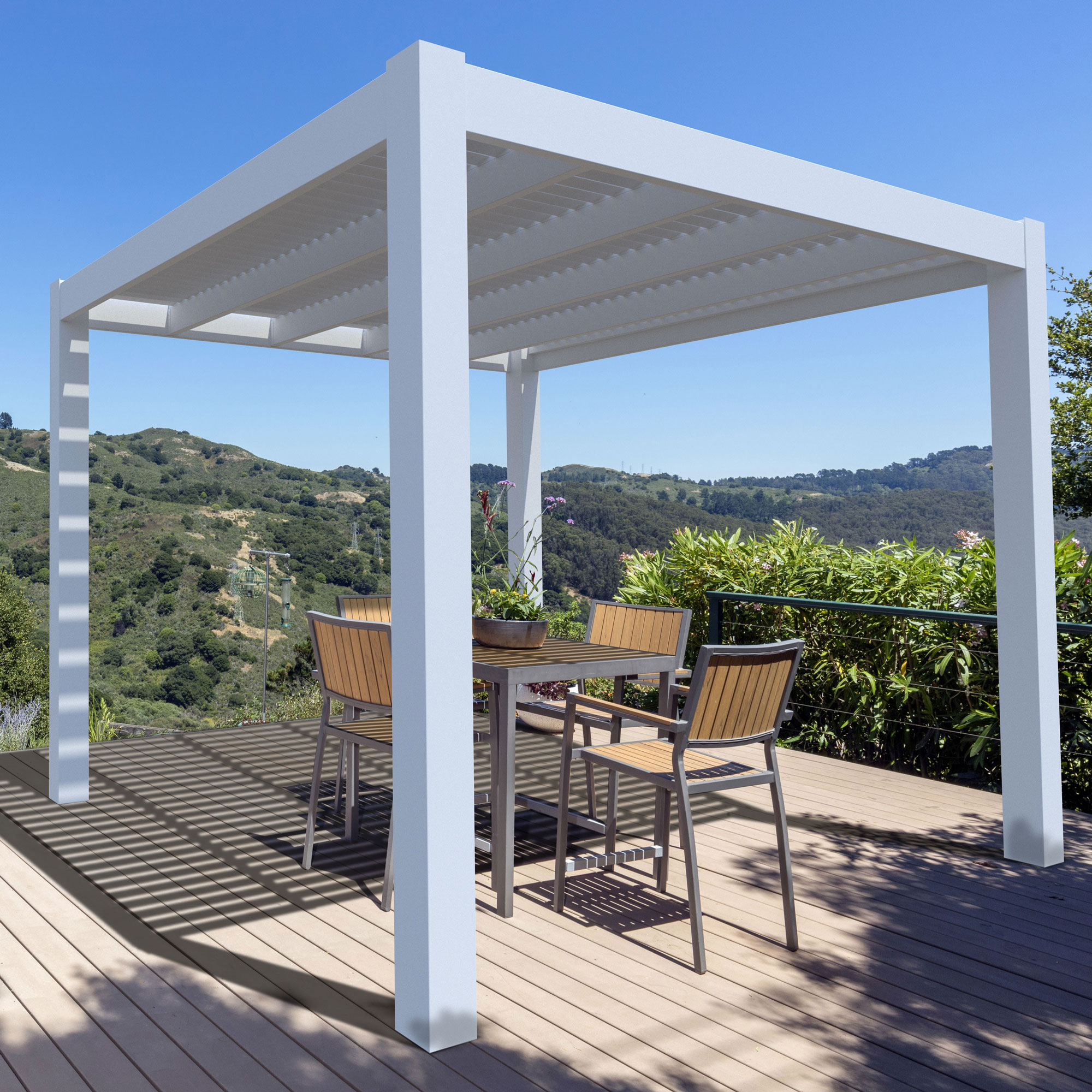 A modern pergola with white siding is covering an outdoor eating area. It overlooks a valley.
