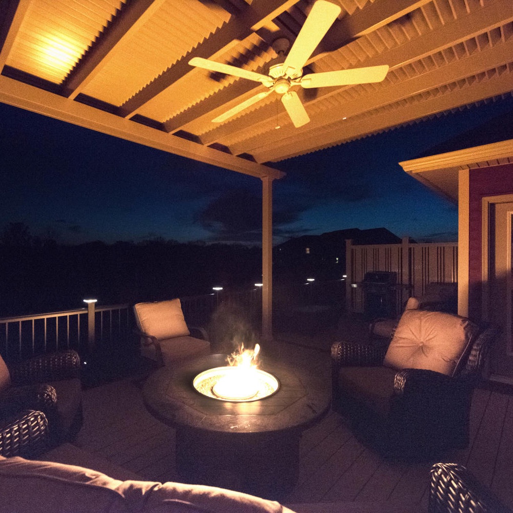 This outdoor seating area has a fire pit centered amongst chairs. It is night, and the fireplace brightens up the space. 