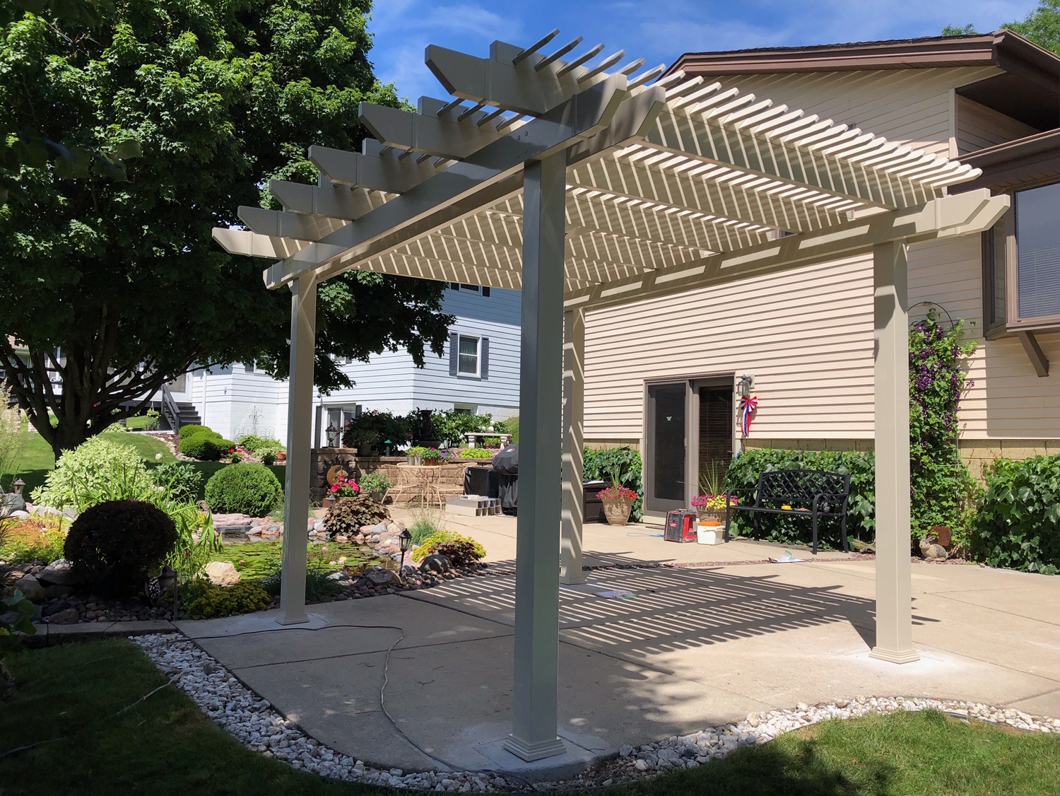 This shaded area has a tan pergola over top of a concrete slab. There isn’t any furniture below the pergola, and it isn’t attached to the home.