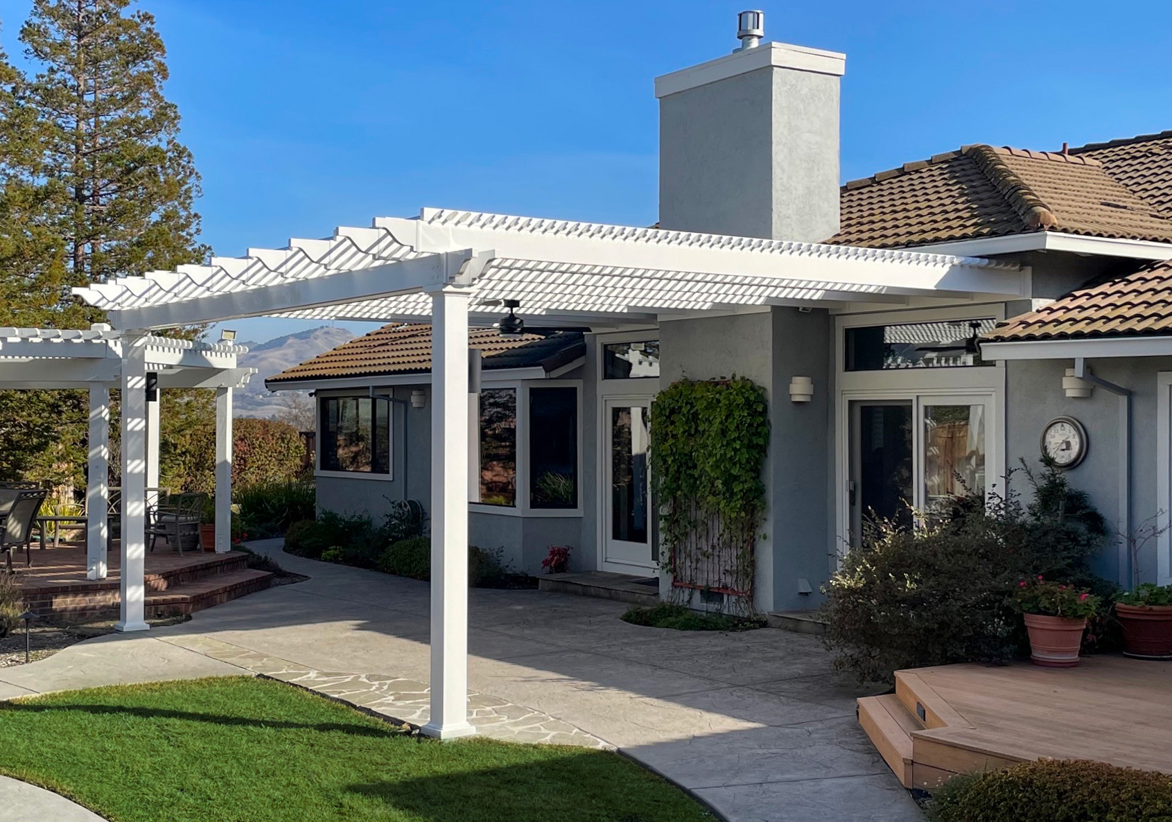 Attached vinyl pergola on a California home over backyard patio with mountains in the background.