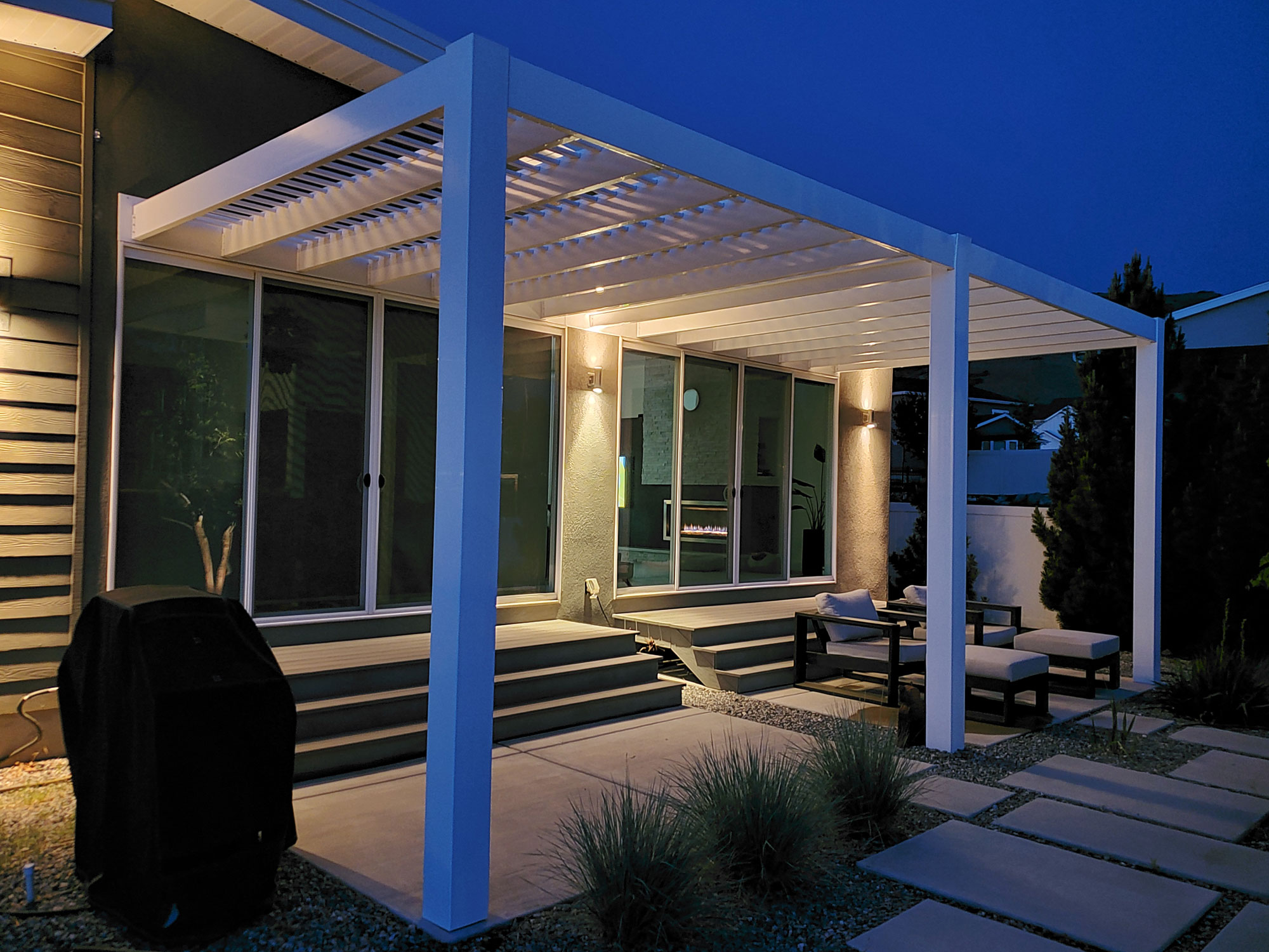 White attached modern pergola over a patio at night with lights