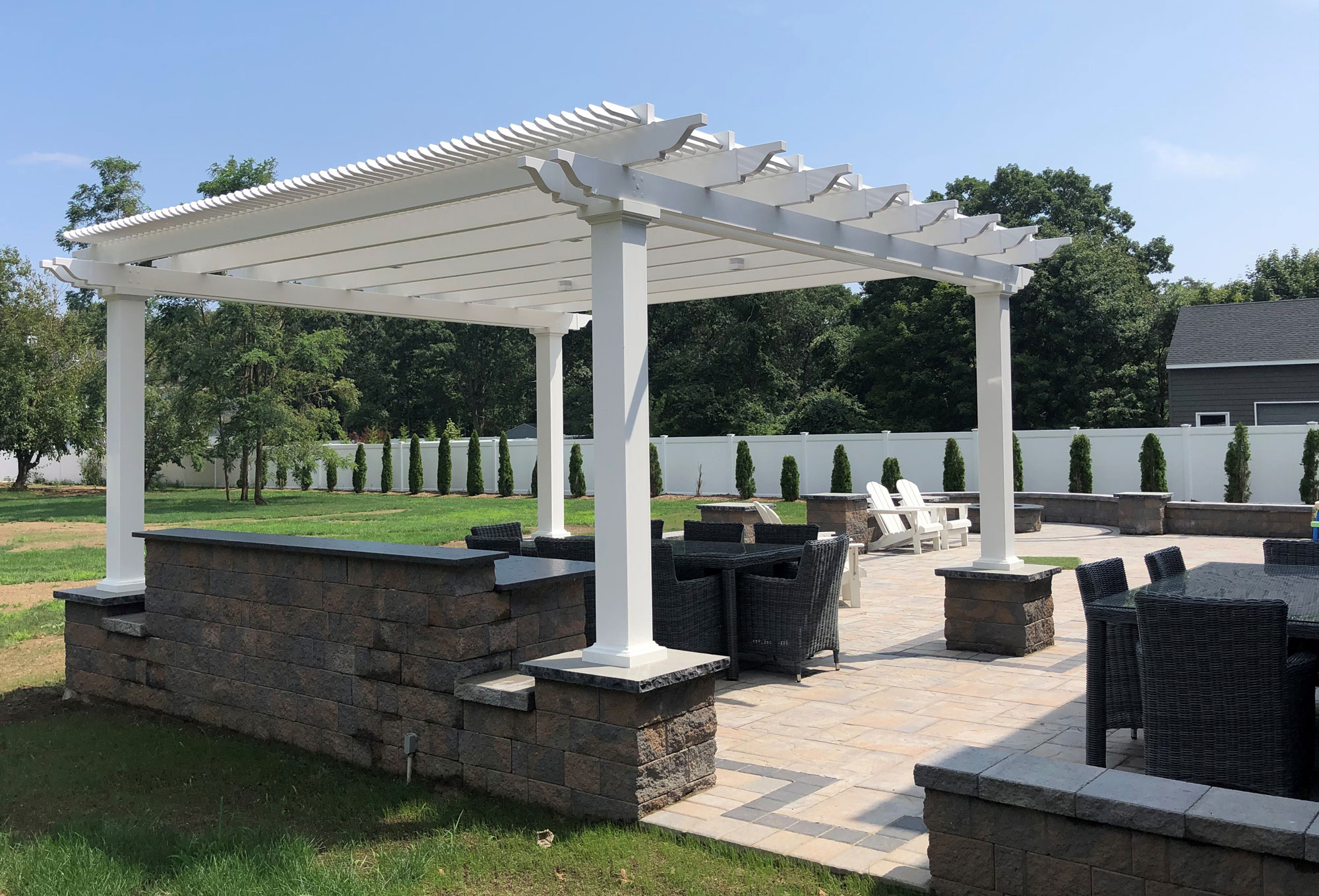 White freestanding pergola on top of landscape columns over a outdoor kitchen and dining area