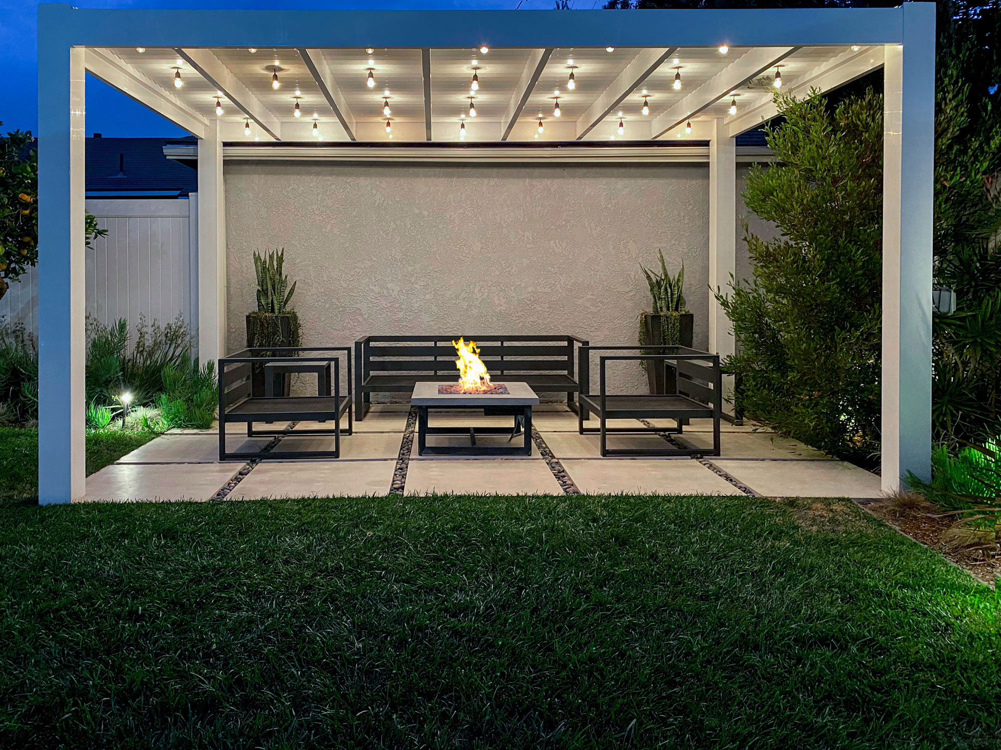 White modern pergola with cantina bistro lights and firepit at night