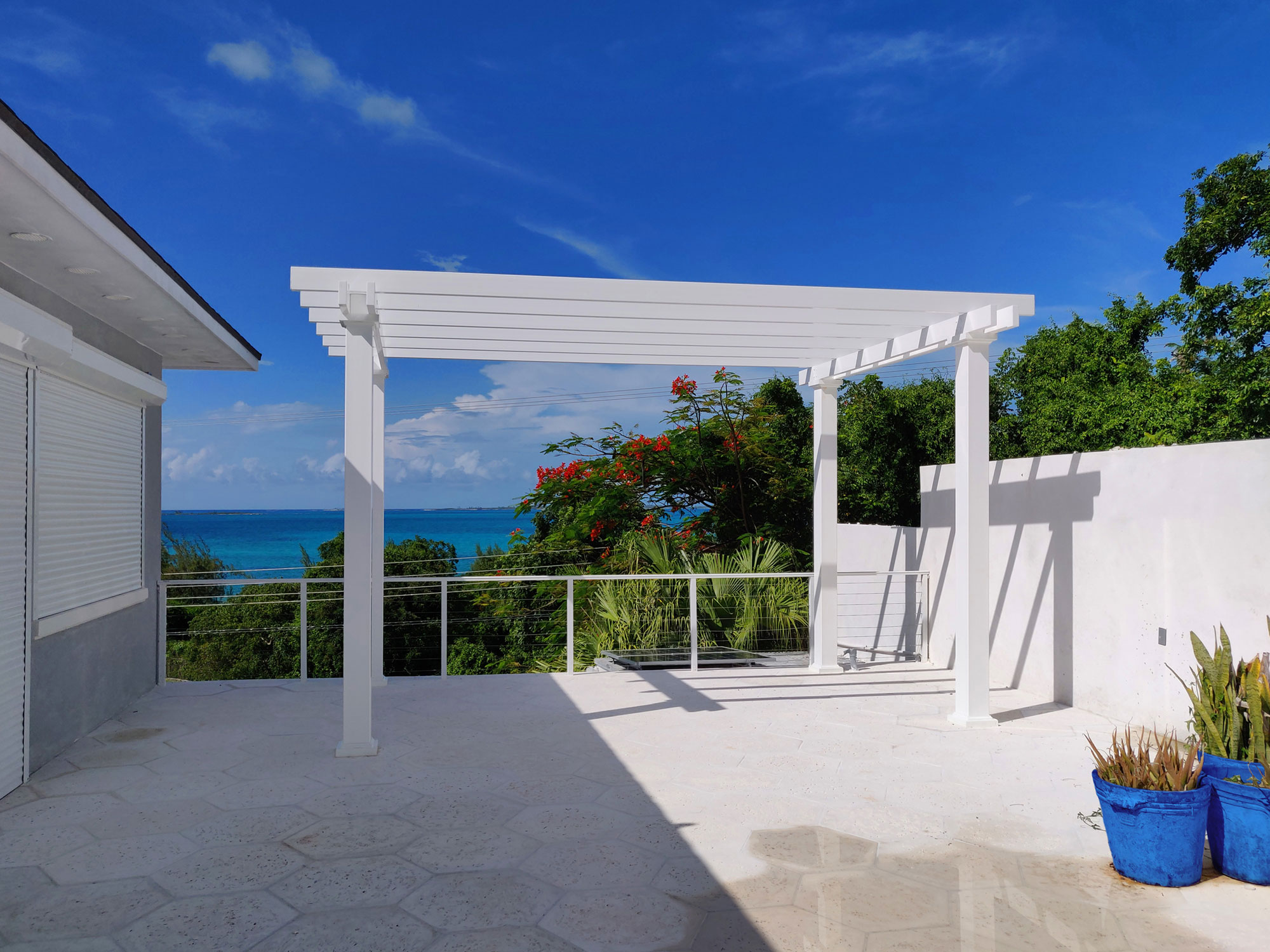 Freestanding white vinyl pergola on a tropical patio. Pergola has no roof just beams for decoration.