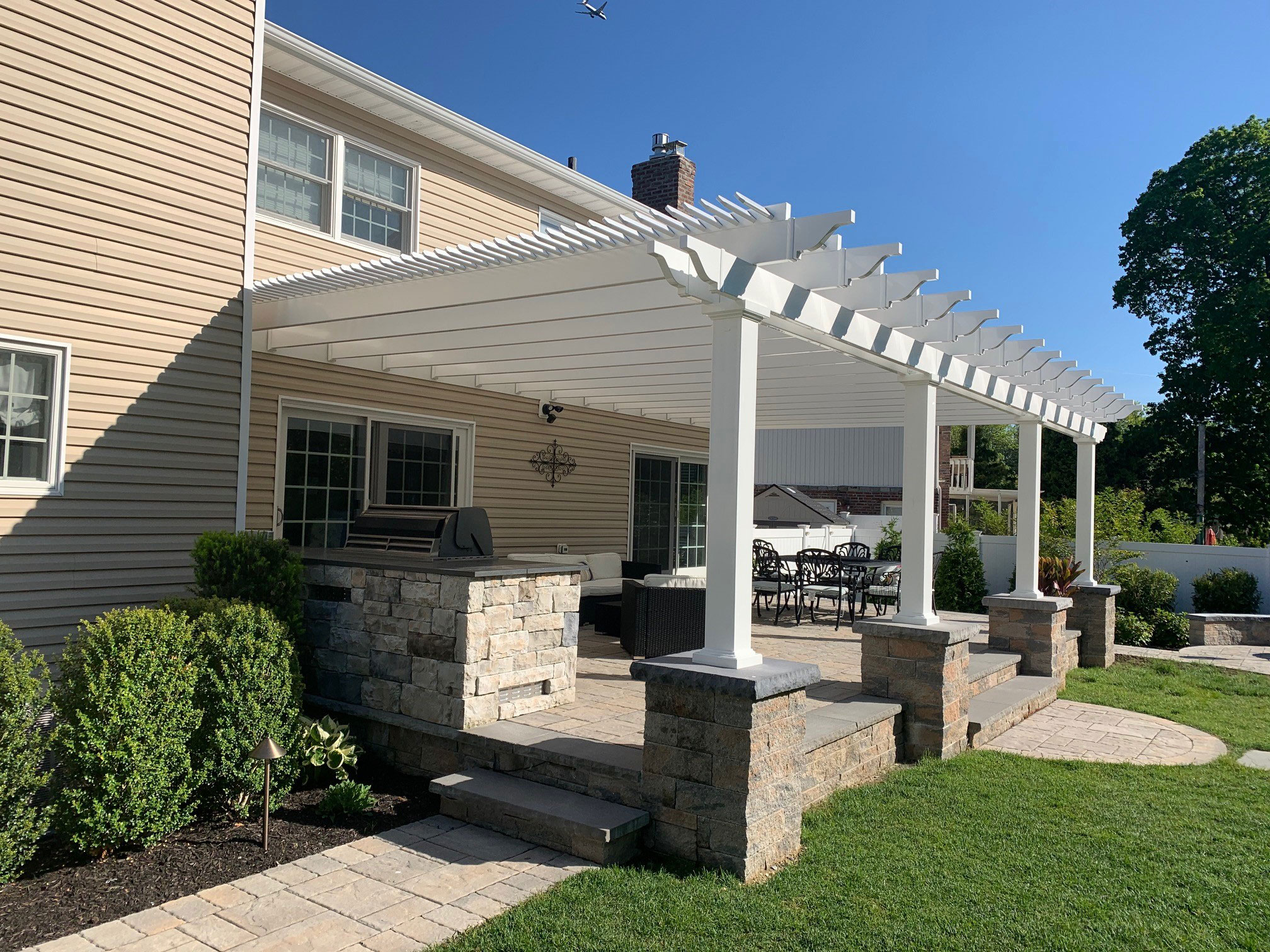 Large white pergola spans the length of a patio seating area providing shade