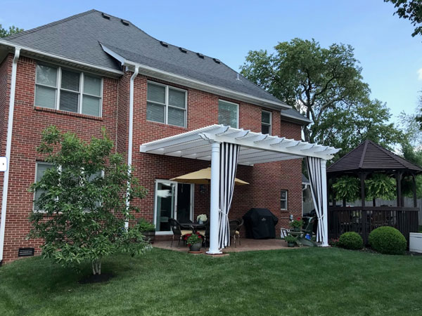 Vinyl Pergola attached to brick home with black & white curtains
