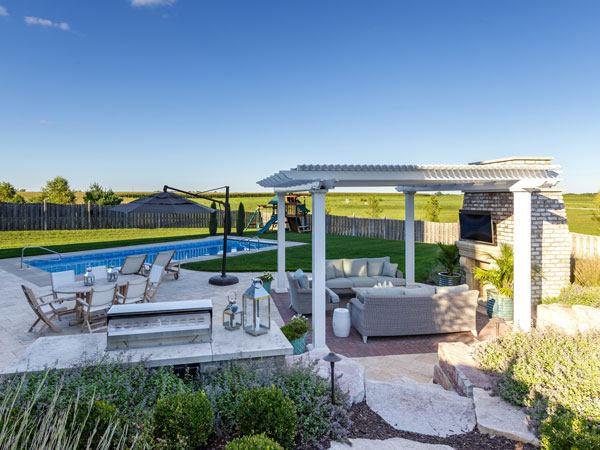 Freestanding pergola next to an outdoor fireplace and backyard pool with seating