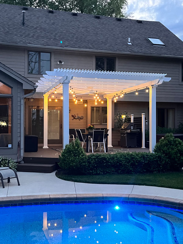 Night time by the pool with a pergola lit up with string lights