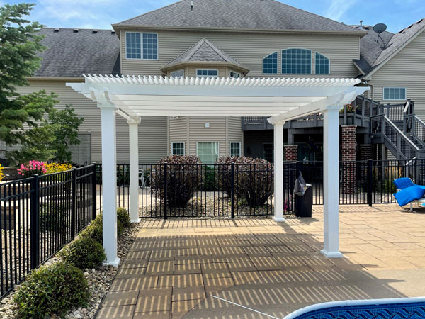 White Vinyl pool side pergola set ontop of stone pavers in a fenced yard