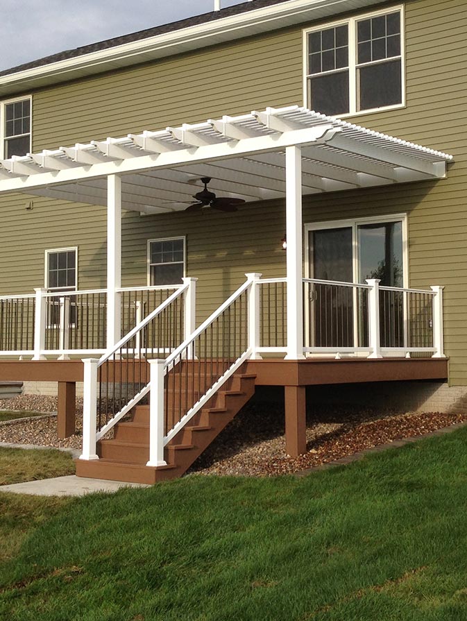 A home with a white pergola over top of the back deck. The pergola is attached to the home and has the outer posts integrated into the deck railings