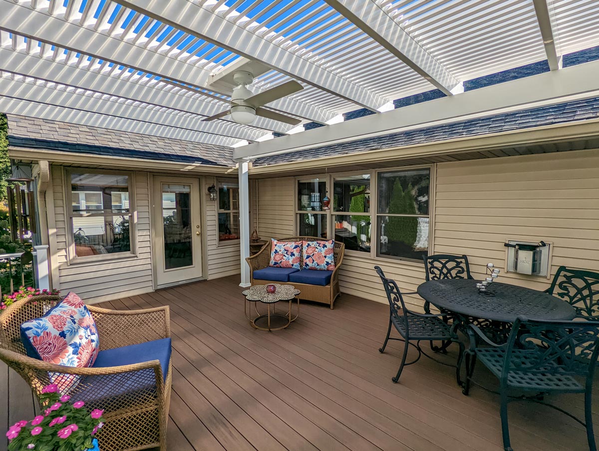 view of a nicely furnished deck attached to a house with a white pergola overhead