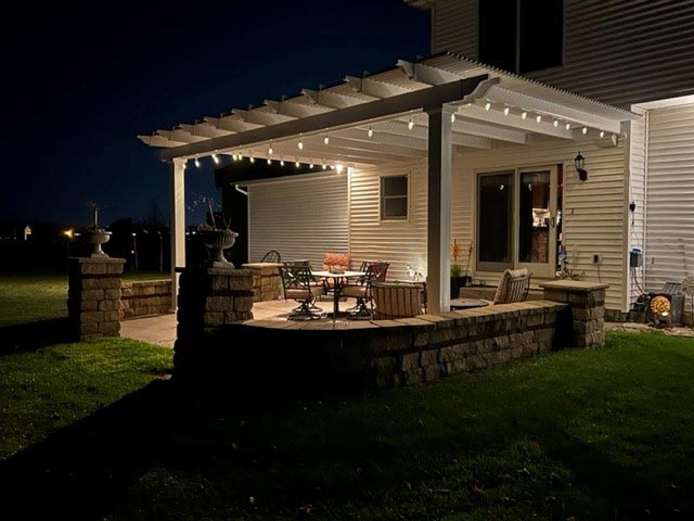 nighttime shot of an attached pergola lit up with bistro lights on a patio