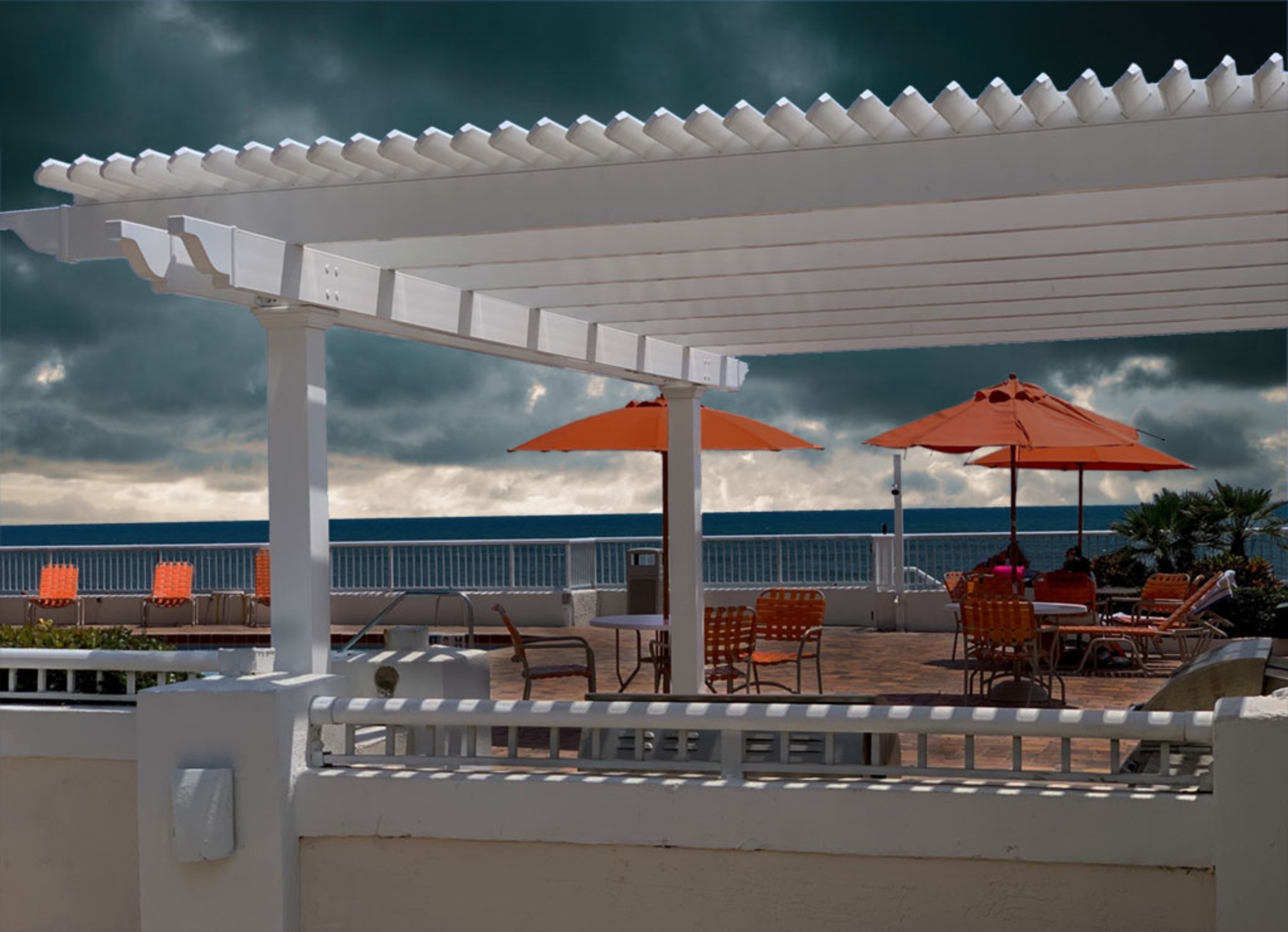 Large white Heartland Pergola on pool deck over looking the ocean and incoming storm