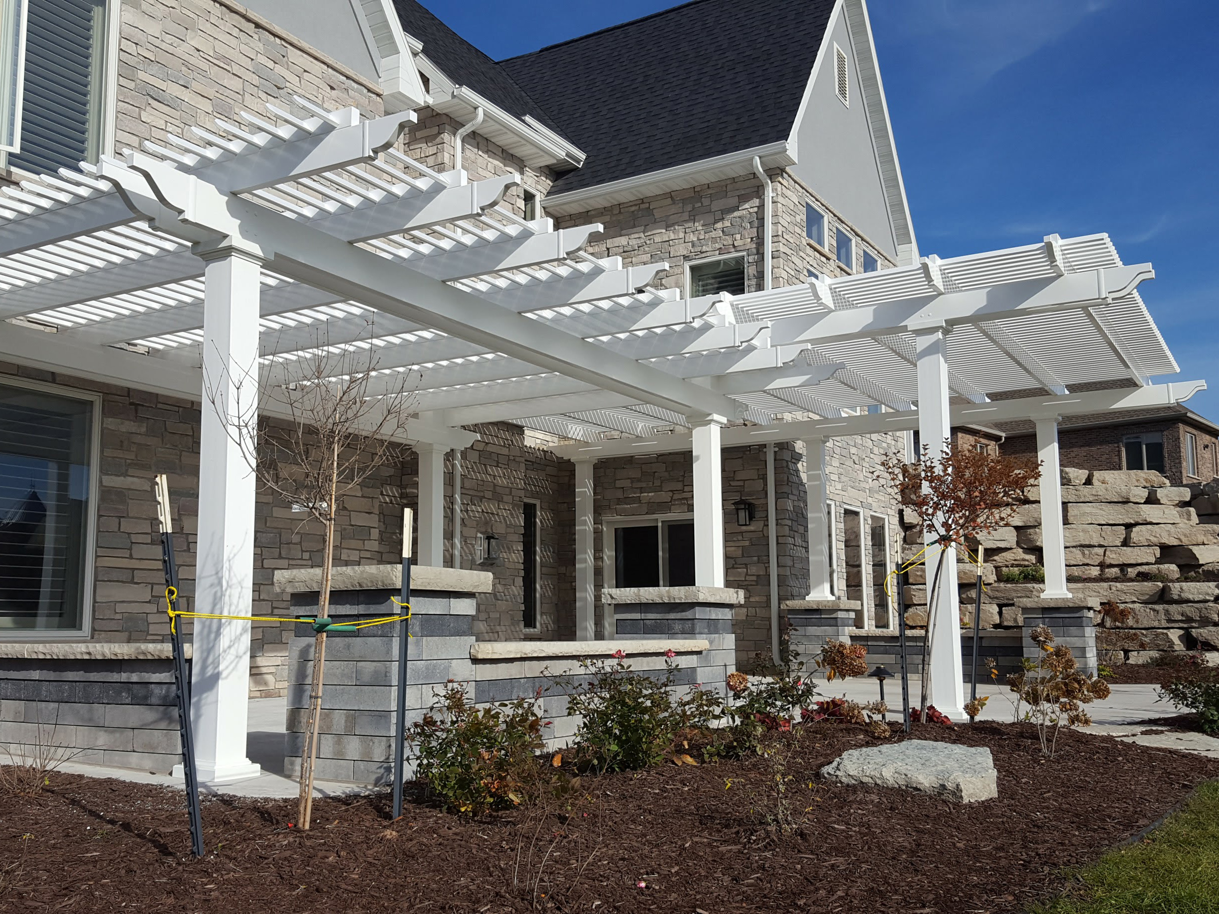 Custom pergola that features a shade structure over an outdoor dining table on one side and attached cutom arbor stretching out over an outdoor grill and kitchen area on the other isde.