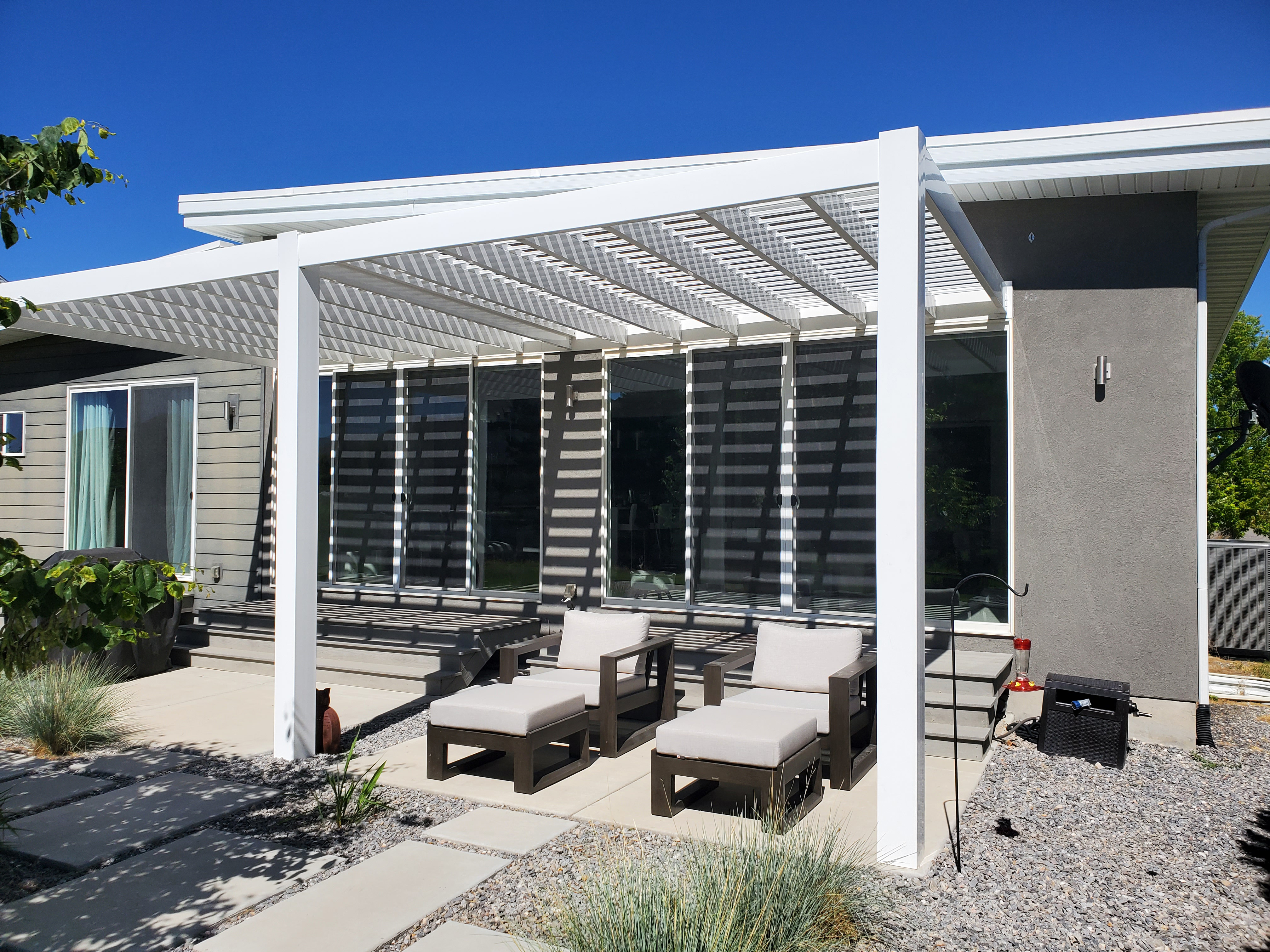 Sleek modern pergola design over a patio and lounge chairs. The pergola is attached to the house.