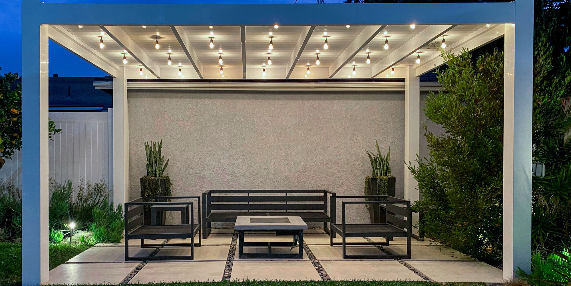 white modern vinyl pergola over a patio at night lit up with bistro lights