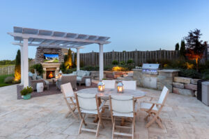 Freestanding white vinyl pergola on a nicely landscaped patio with outdoor fireplace and outdoor seating areas.