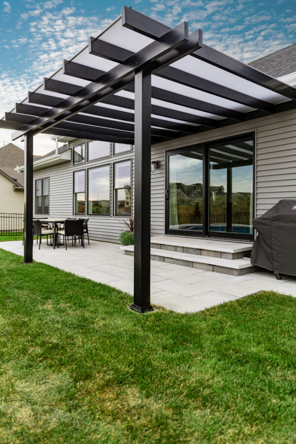 Black rain proof pergola patio cover with white polycarbonate roof over sliding patio doors.