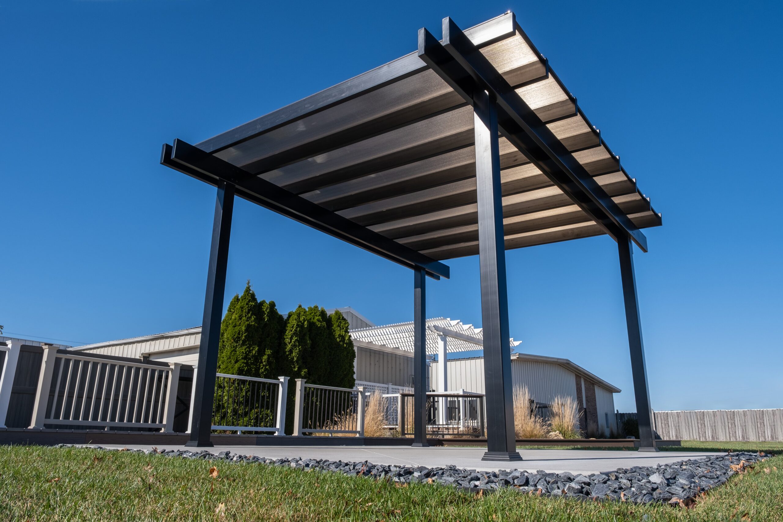 A freestanding patio cover rain proof pergola with bronze polycarbonate roof over patio slab.