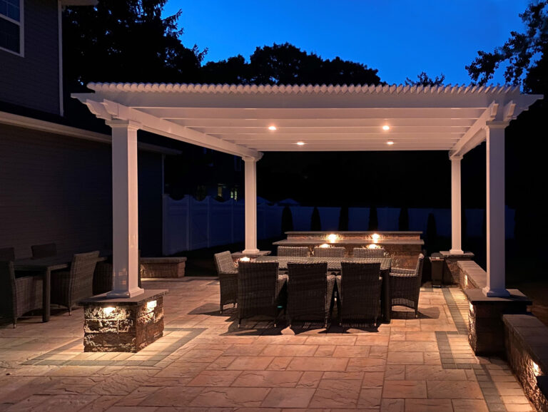 Pergola at night over a paver patio with can lights built into the top of the pergola