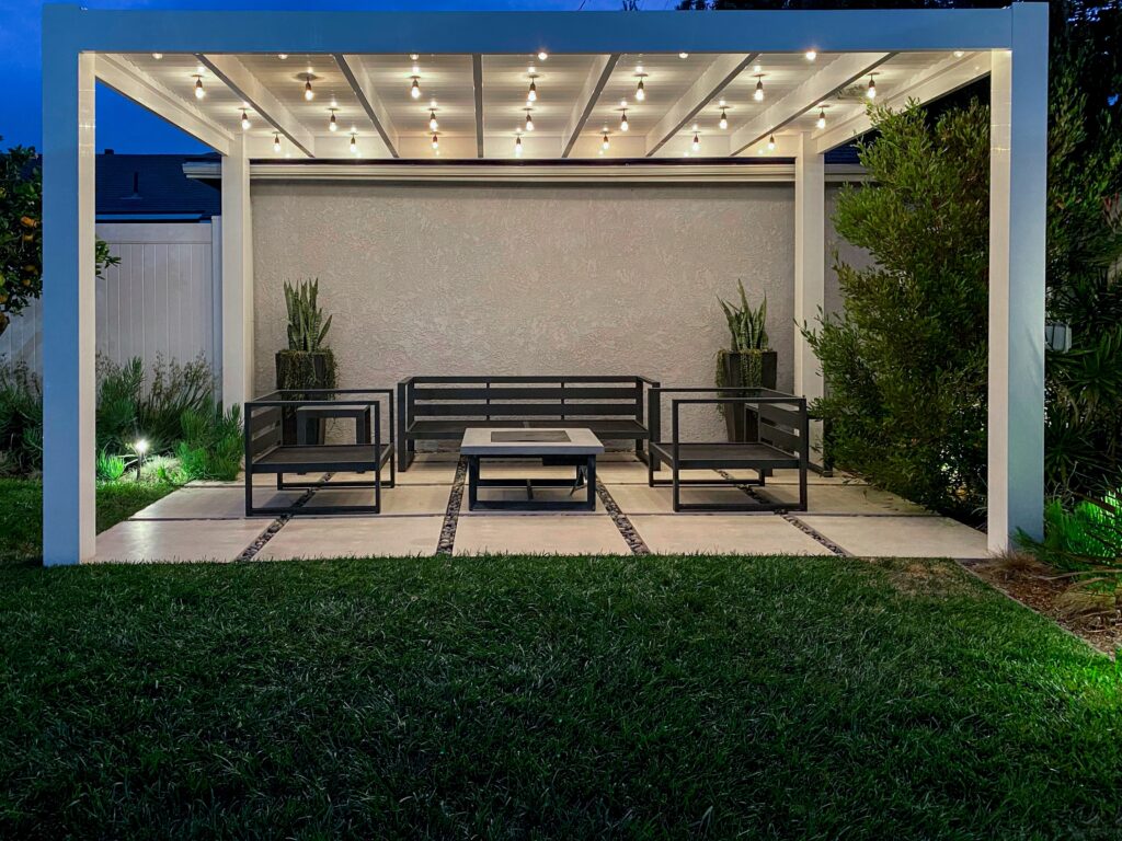 Modern white vinyl pergola over large stone pavers with string lights.