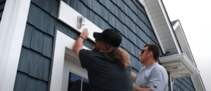Two men installing the ledger board over a garage for an eyebrow pergola installation.