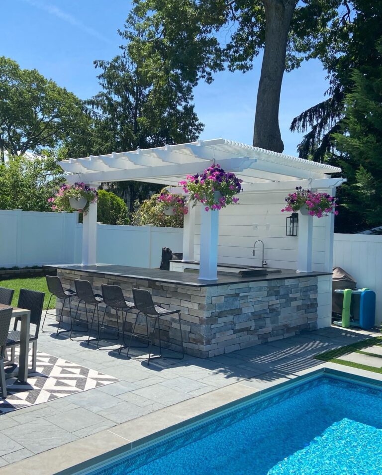Outdoor bar and kitchen area next to a pool with a shade pergola