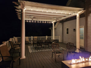 Night time view of a white pergola on a deck with string lights.