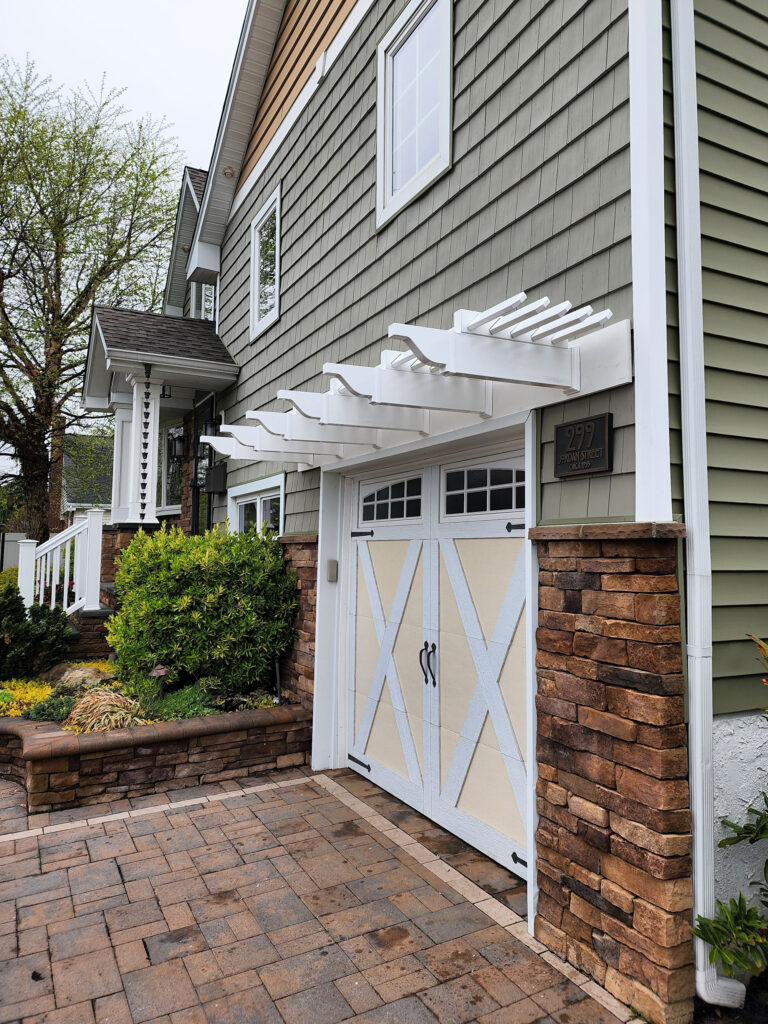 White vinyl eyebrow pergola over a single car garage on the front of a home.