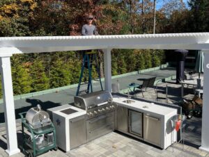 Contractor stands on ladder over a triangle pergola he built over an outdoor kitchen