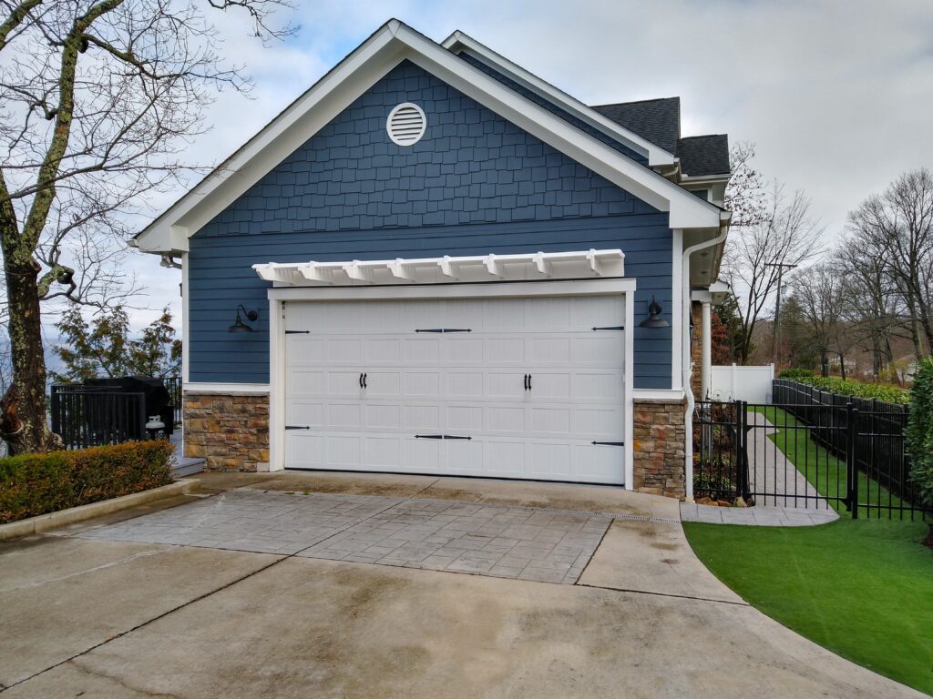 White eyebrow pergola above double garage door on a blue and brick home